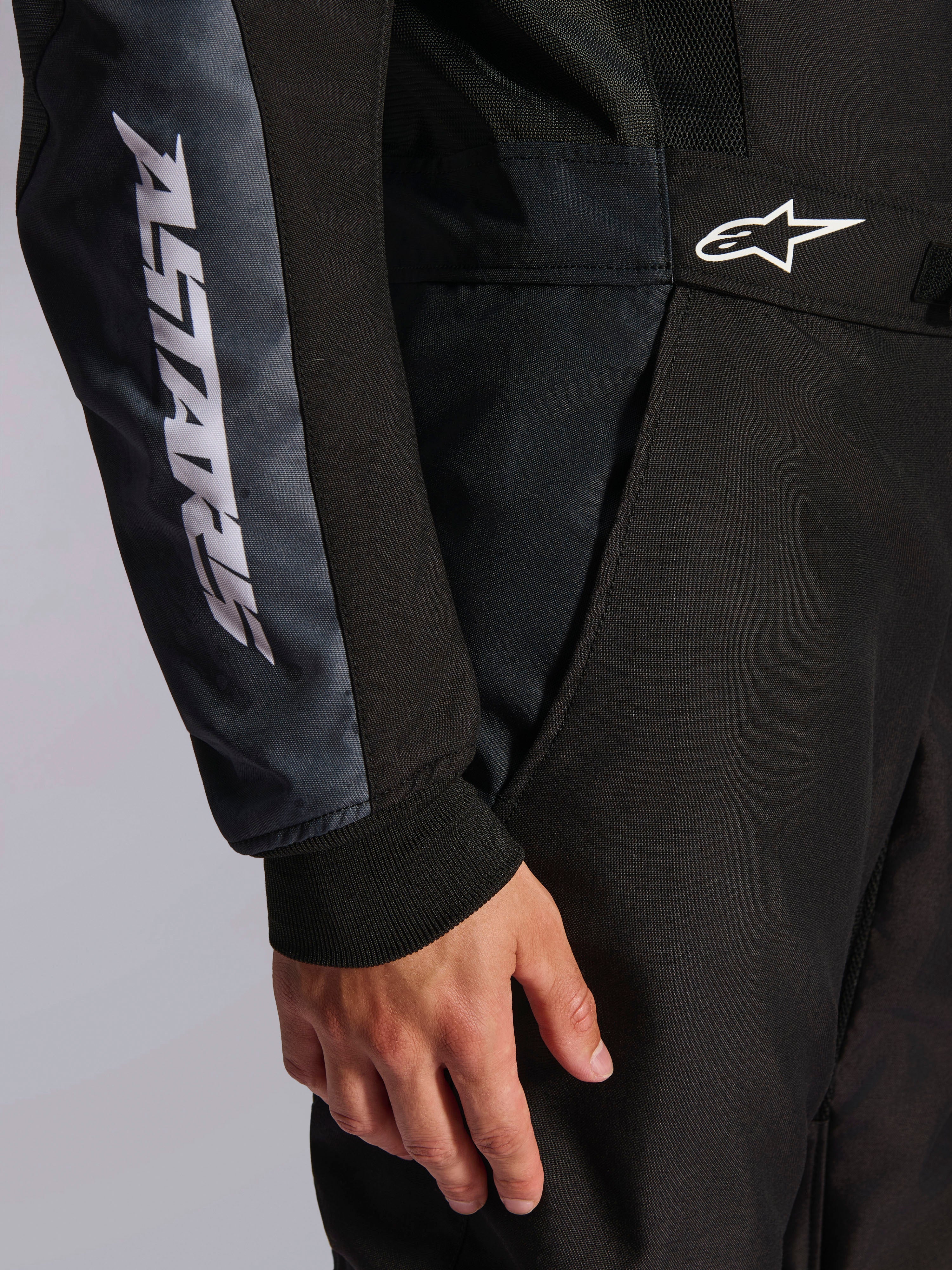 Tuta Alpinestars KMX-5 V3, tuta da kart, nero e Dark Shadow, dettaglio ravvicinato del fianco e del braccio, marchio ASTARS bianco sulla manica, logo bianco in vita, con pannelli in mesh per la ventilazione e polsino in maglia