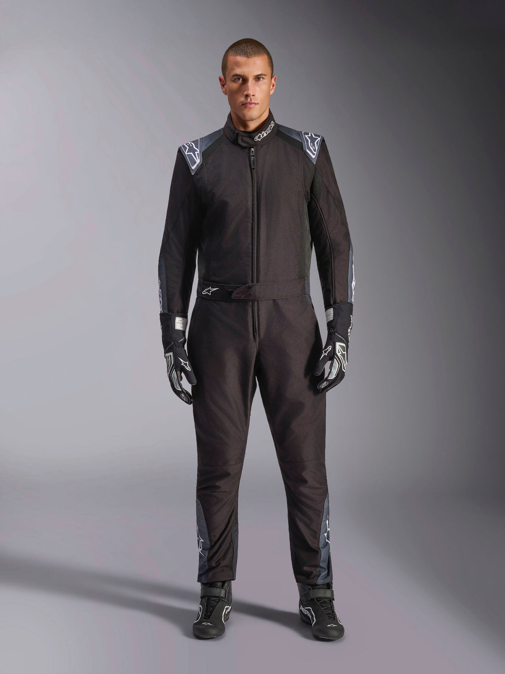 Tuta Alpinestars KMX-5 V3, tuta da karting, Nero Dark Shadow, vista a figura intera di un modello che indossa la tuta con guanti e stivali coordinati, caratterizzata da dettagli grigio scuro e loghi Alpinestars bianchi su spalle e cintura, abbigliamento professionale per sport motoristici.