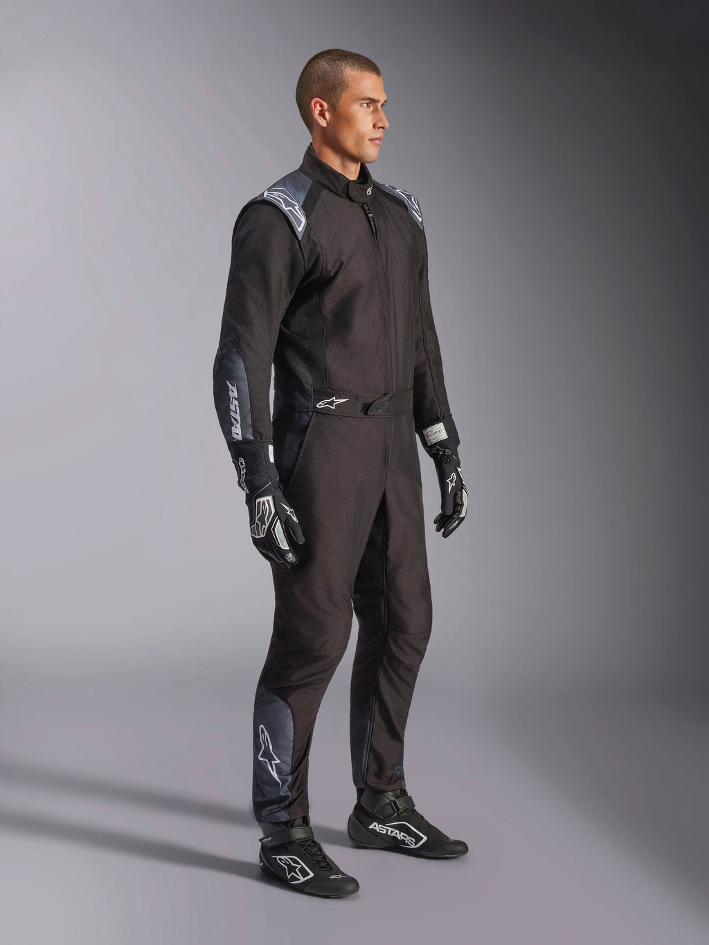 Tuta Alpinestars KMX-5 V3, tuta da kart in nero Dark Shadow, indossata con guanti e scarpe da corsa neri coordinati, dotata di traforazioni tagliate al laser e pannelli in mesh tecnico, elegante design a doppio strato con loghi bianchi per il motorsport professionale