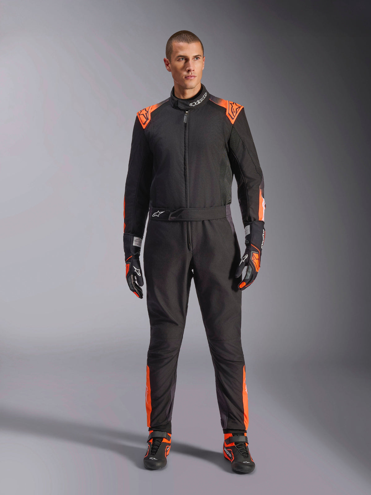 Tuta Alpinestars KMX-5 V3 da uomo, nera e arancione fluo, certificata FIA, indossata con guanti e scarpe coordinati.