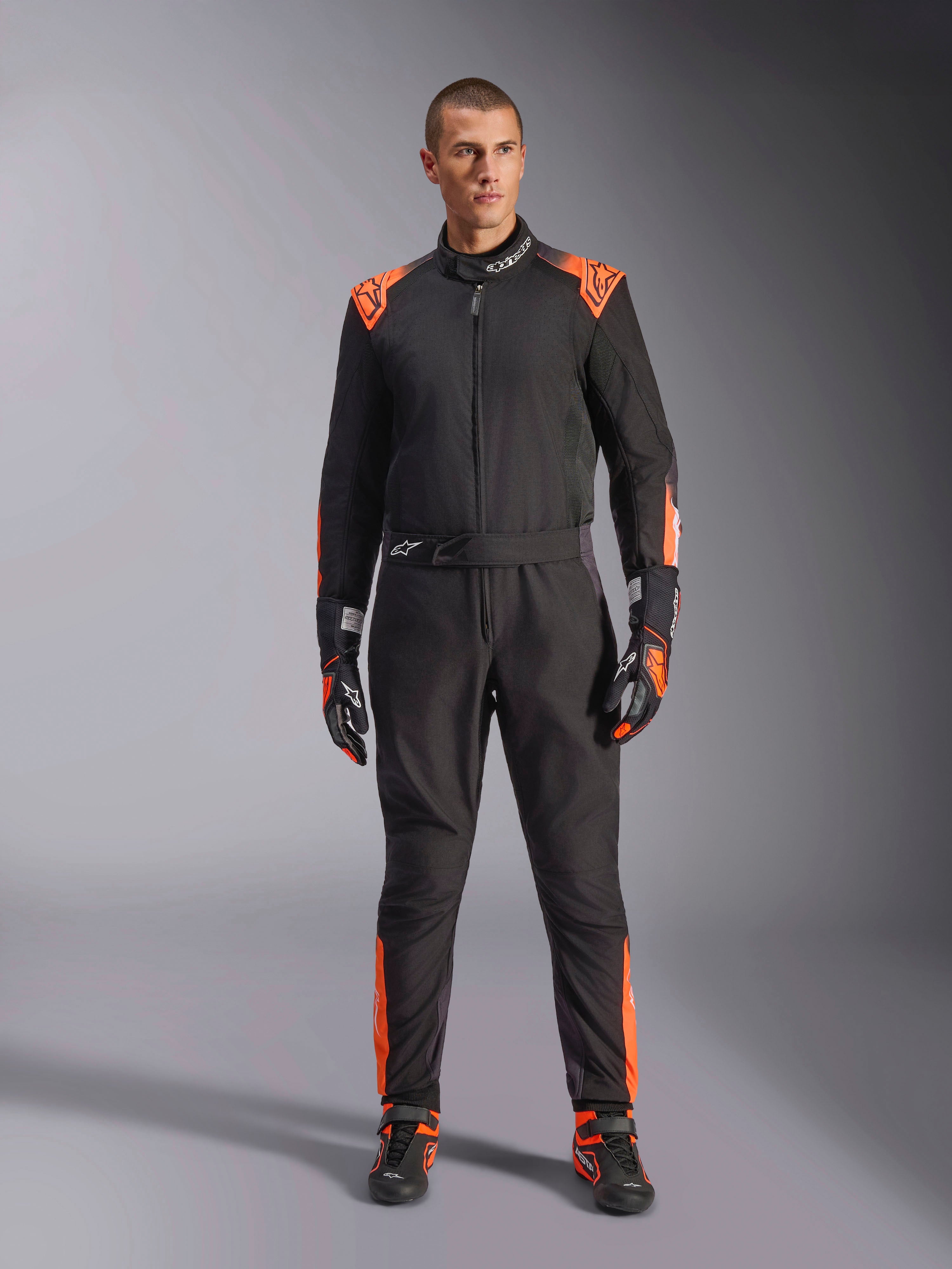 Tuta Alpinestars KMX-5 V3 da uomo, nera e arancione fluo, certificata FIA, indossata con guanti e scarpe coordinati.