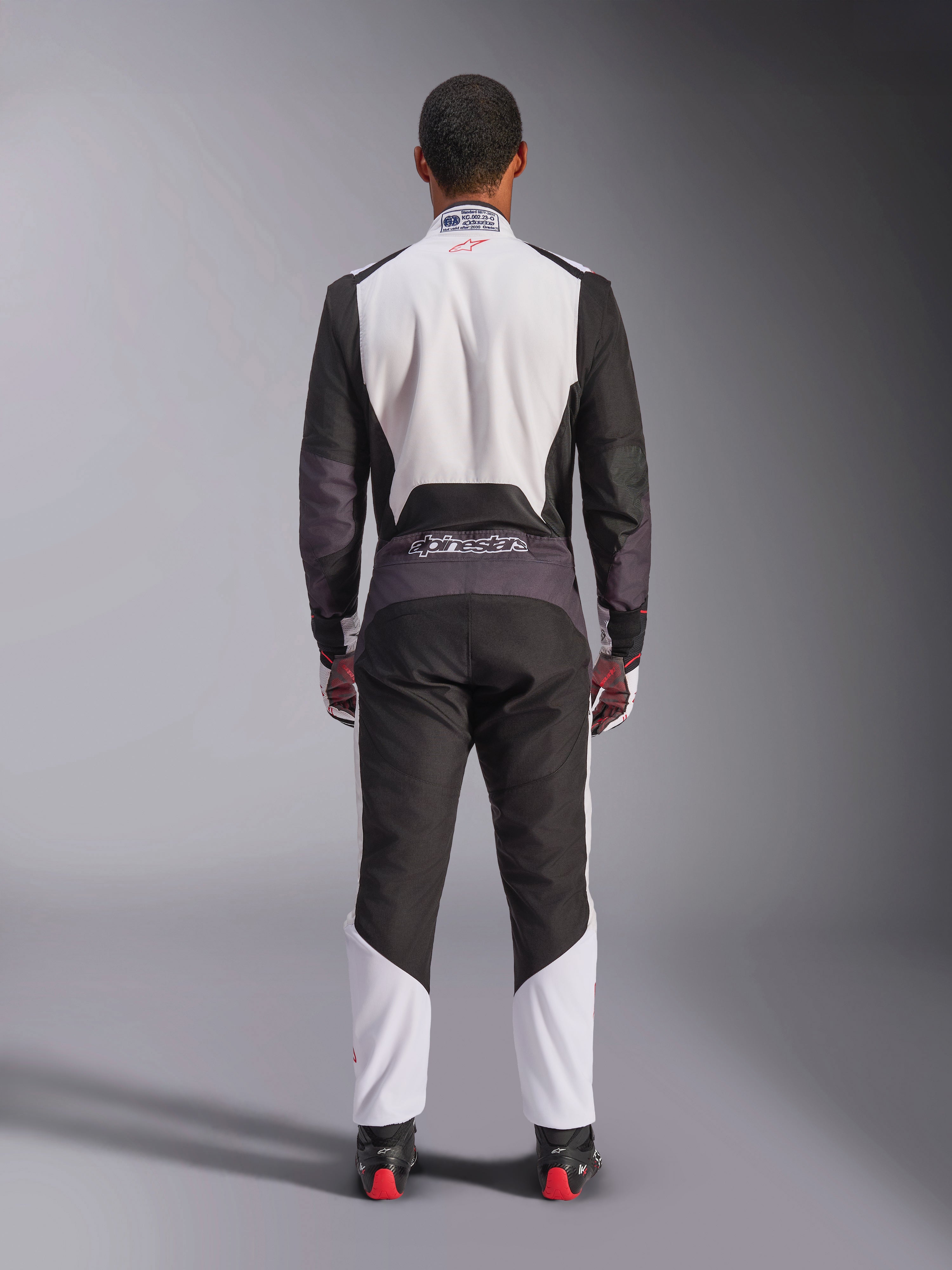 Tuta Alpinestars KMX-5 V3, tuta da karting, bianco, nero e rosso vivace, vista posteriore, tuta da corsa intera con pannelli in mesh traspirante e logo Alpinestars sulla vita, indossata con guanti e stivali da corsa coordinati