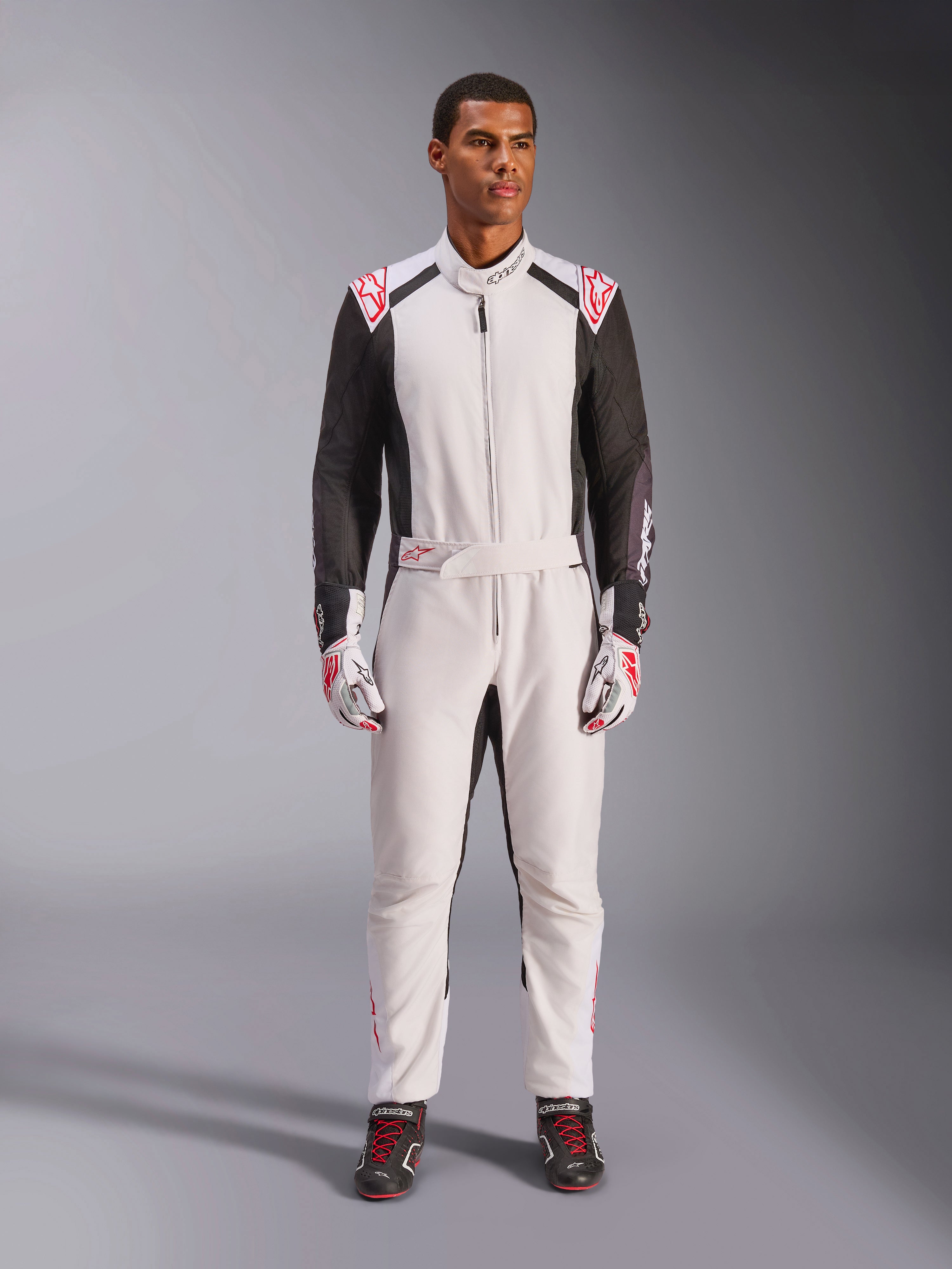Tuta Alpinestars KMX-5 V3, tuta da kart intera, bianco, nero e rosso brillante, indossata da un modello con guanti e scarpe da corsa coordinati, abbigliamento professionale da motorsport per la guida competitiva di go-kart.