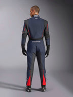Vista posteriore della Tuta Alpinestars GP Tech V4 in Blu Navy Nero Rosso, tuta intera da corsa auto con pannelli elasticizzati neri e accenti rossi, marchio Alpinestars e dettagli di certificazione FIA, indossata con guanti e stivali da corsa professionali.