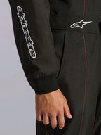 Primo piano della tuta Alpinestars KMX-9 V3 in Nero e Rosso Fluo, caratterizzata dal marchio Alpinestars ricamato in bianco sulla manica, un polsino in maglia e una cintura in vita con logo Astars e cuciture rosse a contrasto.