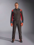 Tuta da Kart Alpinestars KMX-9 V3, nero e rosso fluo, tuta intera da corsa indossata con guanti e stivali coordinati, vivaci inserti rossi sulle spalle e cuciture, logo Alpinestars sulla parte inferiore delle gambe, design motorsport per corse in pista