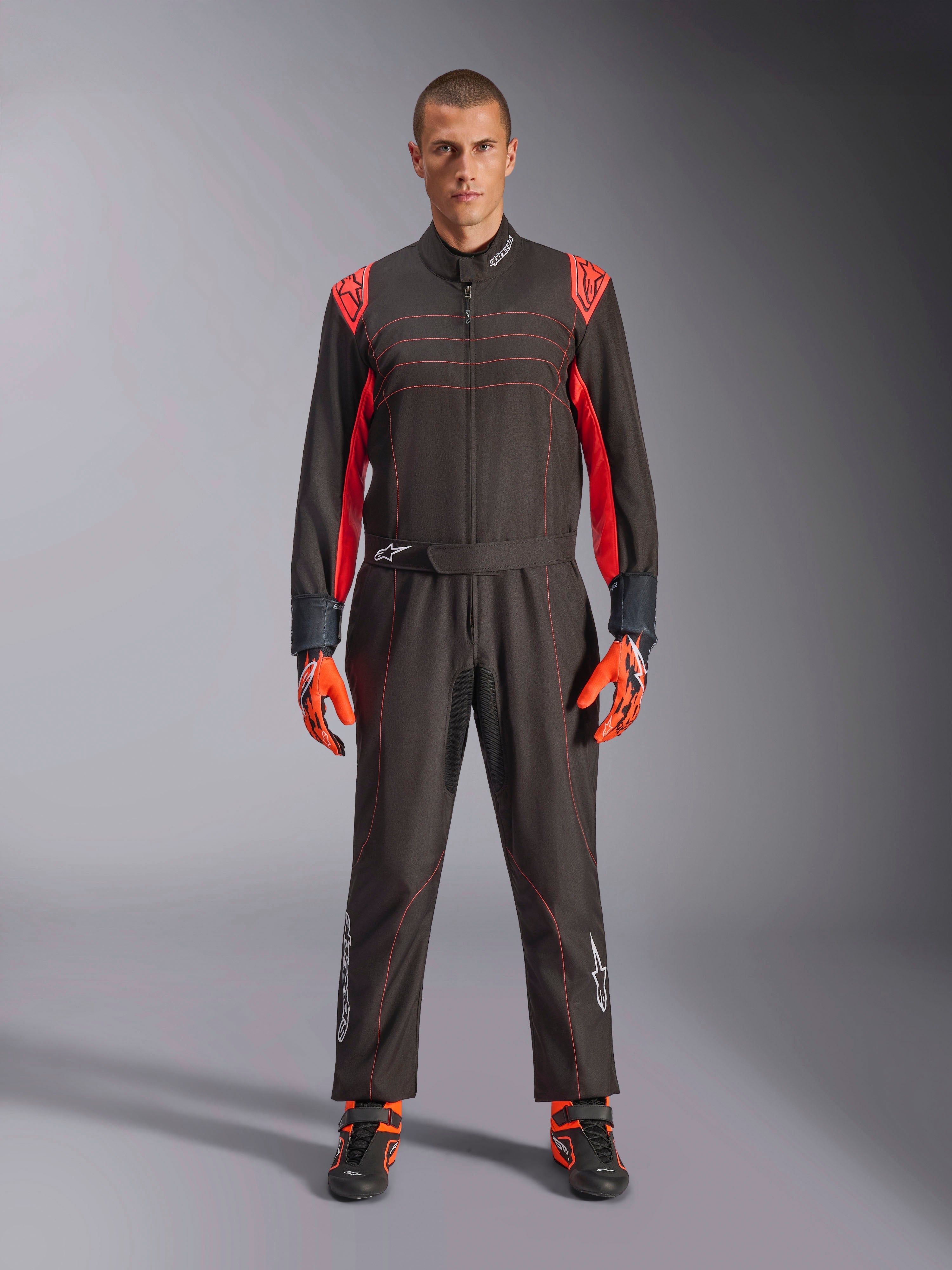 Tuta da Kart Alpinestars KMX-9 V3, nero e rosso fluo, tuta intera da corsa indossata con guanti e stivali coordinati, vivaci inserti rossi sulle spalle e cuciture, logo Alpinestars sulla parte inferiore delle gambe, design motorsport per corse in pista