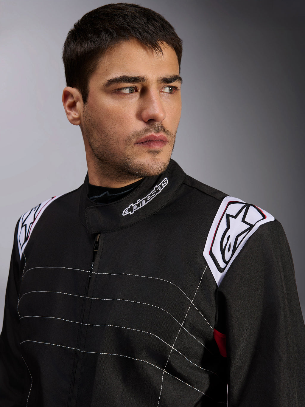 Tuta Alpinestars KMX-9 V3, tuta da kart nera indossata da un modello, primo piano di petto e spalle con logo bianco su colletto e spalline, cuciture decorative bianche e design professionale da motorsport