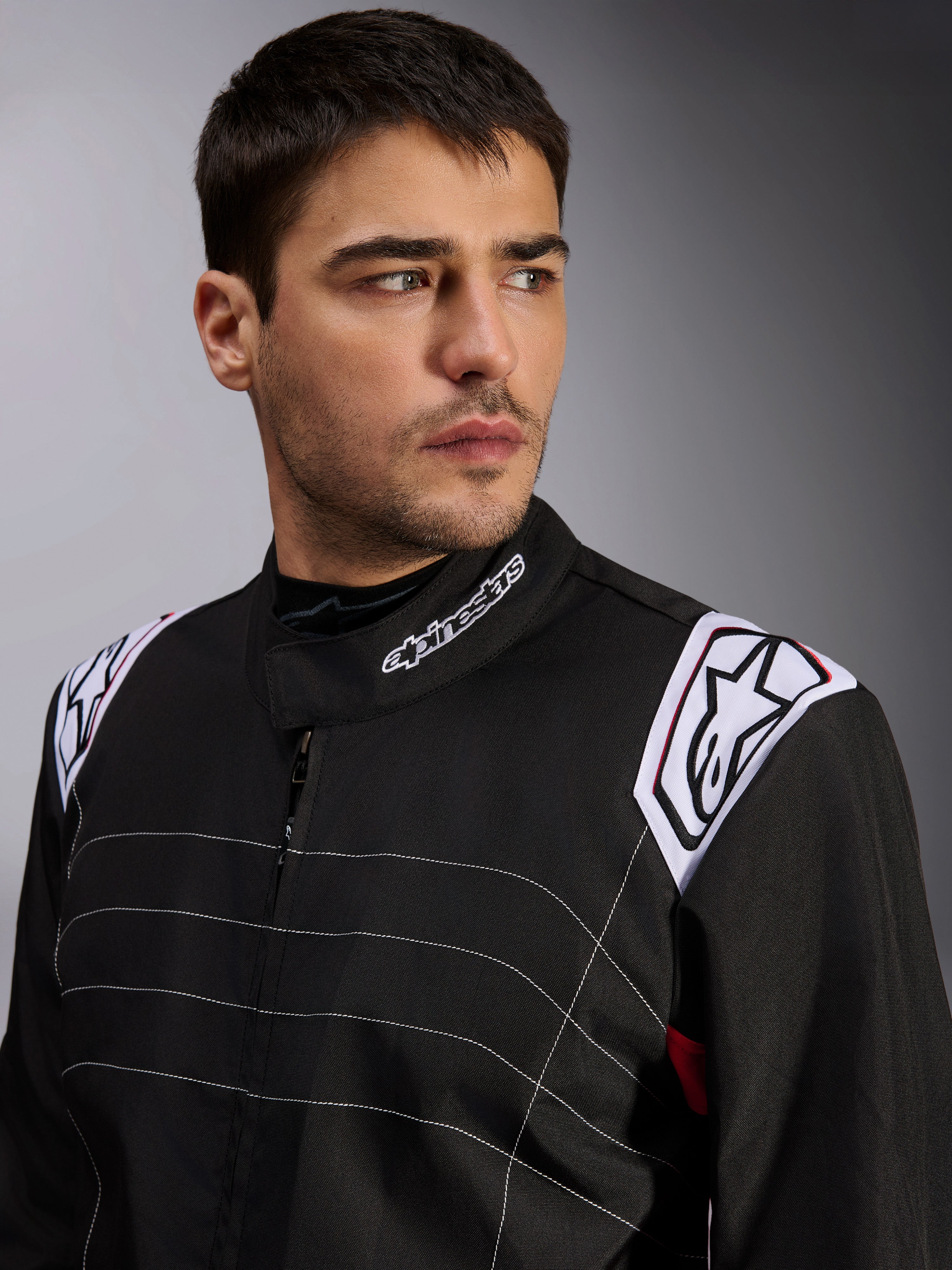 Tuta Alpinestars KMX-9 V3, tuta da kart nera indossata da un modello, primo piano di petto e spalle con logo bianco su colletto e spalline, cuciture decorative bianche e design professionale da motorsport