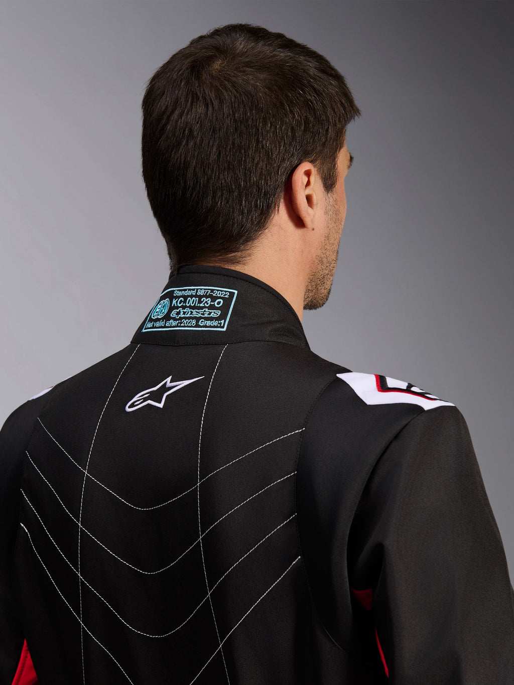 Tuta Alpinestars KMX-9 V3, tuta da karting, nero rosso bianco, vista posteriore del colletto che mostra l'etichetta di omologazione FIA 8877-2022, logo Astars bianco e dettagli delle cuciture decorative