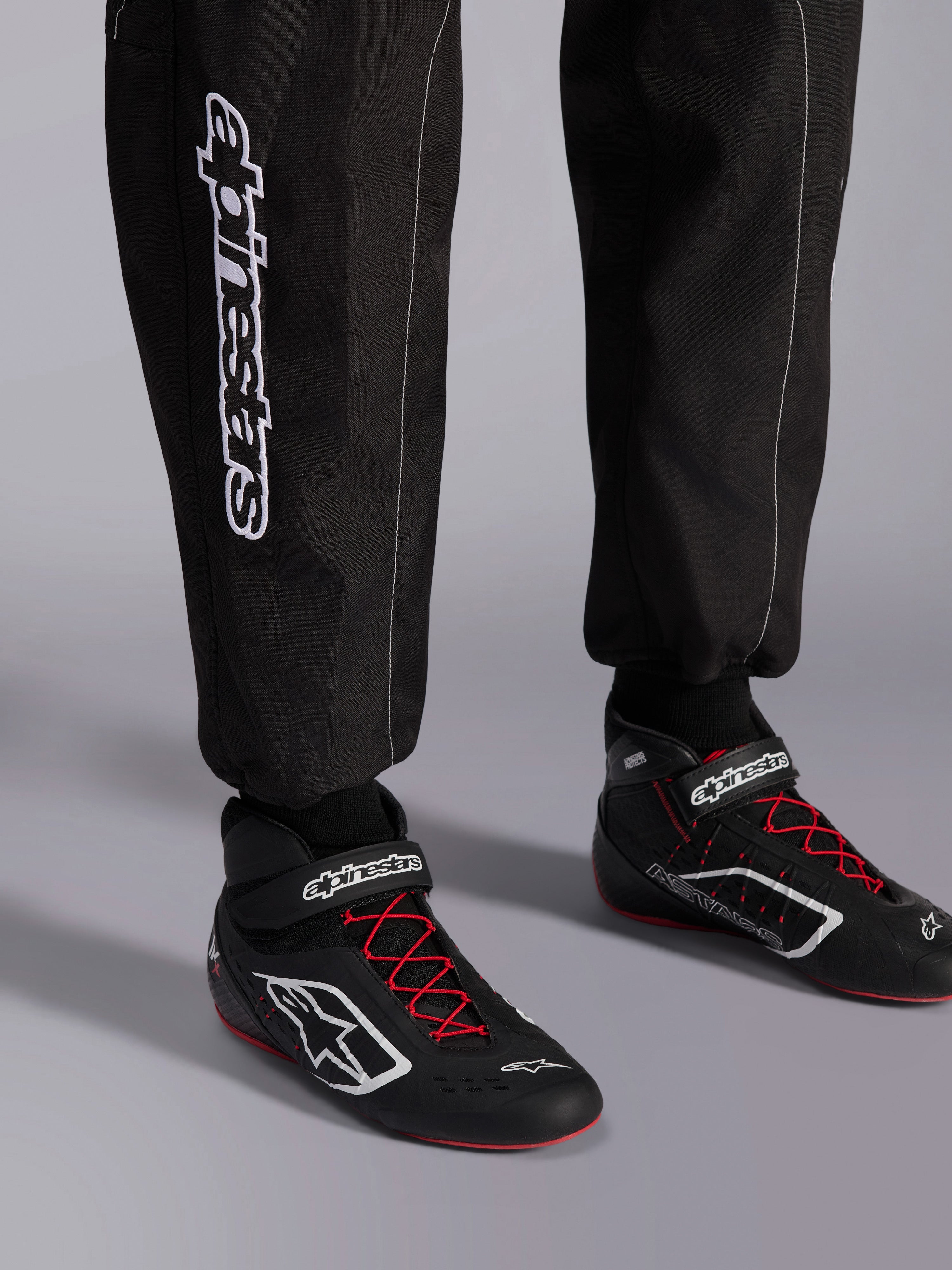 Tuta Alpinestars KMX-9 V3, tuta da kart, nero rosso e bianco, vista dettagliata della parte inferiore delle gambe e degli stivali da kart, branding Alpinestars bianco sul lato, scarpe nere con lacci rossi e accenti bianchi, abbigliamento professionale per competizioni motoristiche
