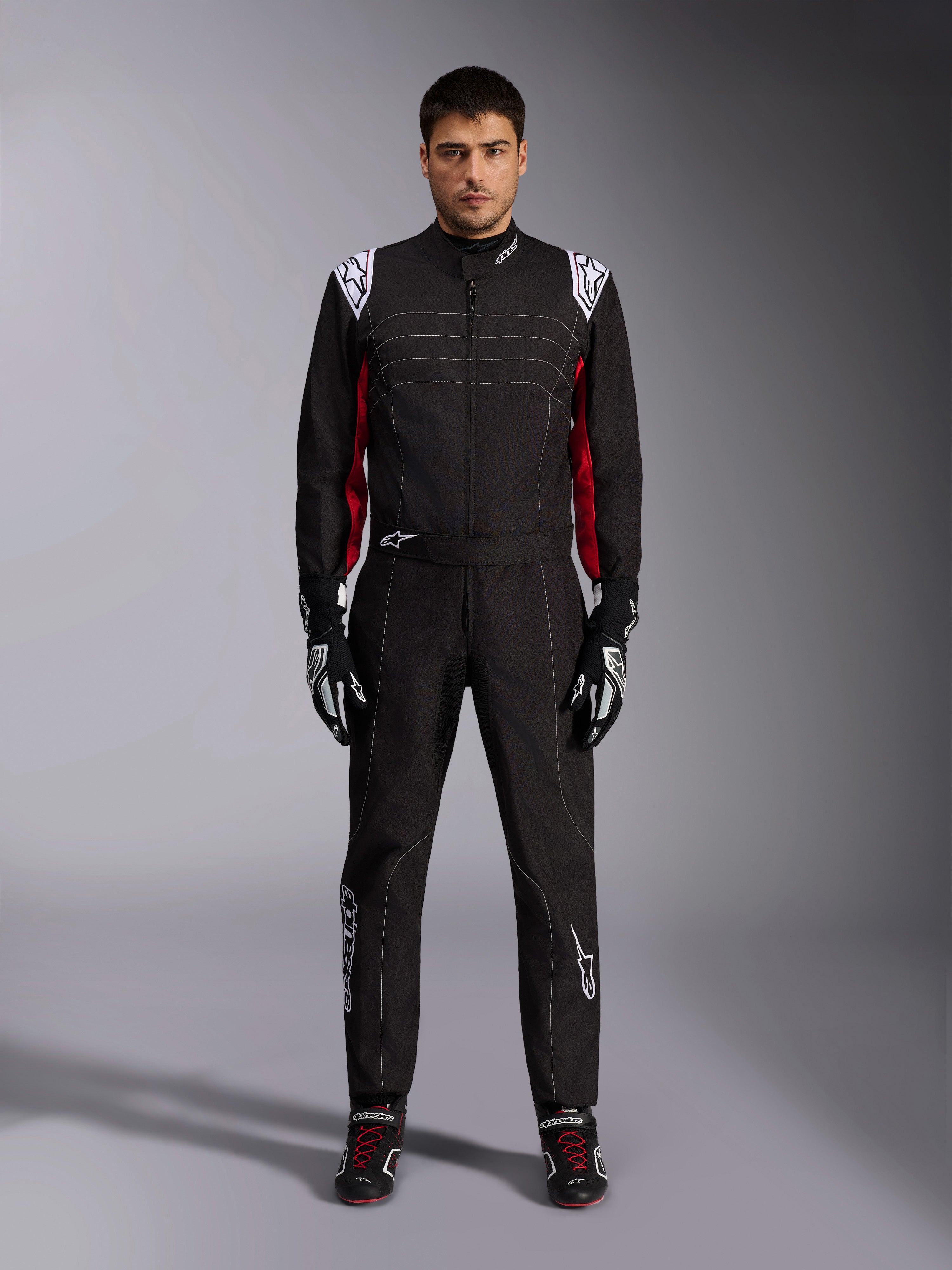 Tuta da kart Alpinestars KMX-9 V3 in nero, rosso e bianco, vista frontale a figura intera di un modello che indossa la tuta intera con guanti e scarpe da corsa coordinati, con loghi Alpinestars bianchi sulle spalle e dettagli rossi.