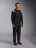 Tuta da karting Alpinestars KMX-9 V3, nero e bianco, modello maschile che indossa la tuta da corsa completa con logo Alpinestars bianco sulle spalline, abbinata a guanti da corsa bianchi e neri e scarpe da kart nere con lacci rossi, scatto in studio che mostra il profilo frontale e laterale