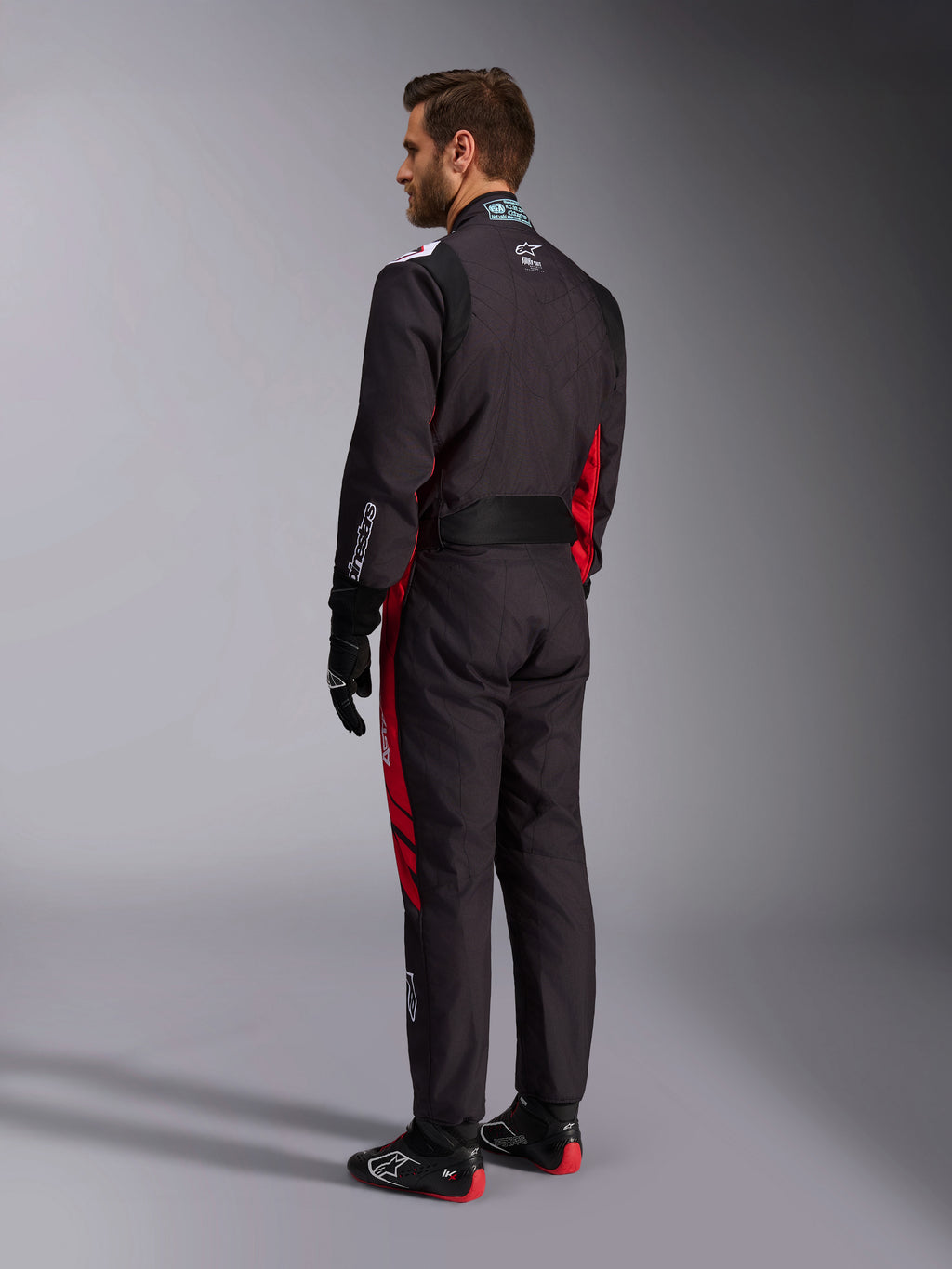 Alpinestars KMX-9 V3 Graphic 3 Suit, nero e rosso, vista posteriore del modello con attrezzatura completa da kart inclusi guanti neri e stivali da corsa, con pannelli laterali rossi e dettagli del logo bianchi