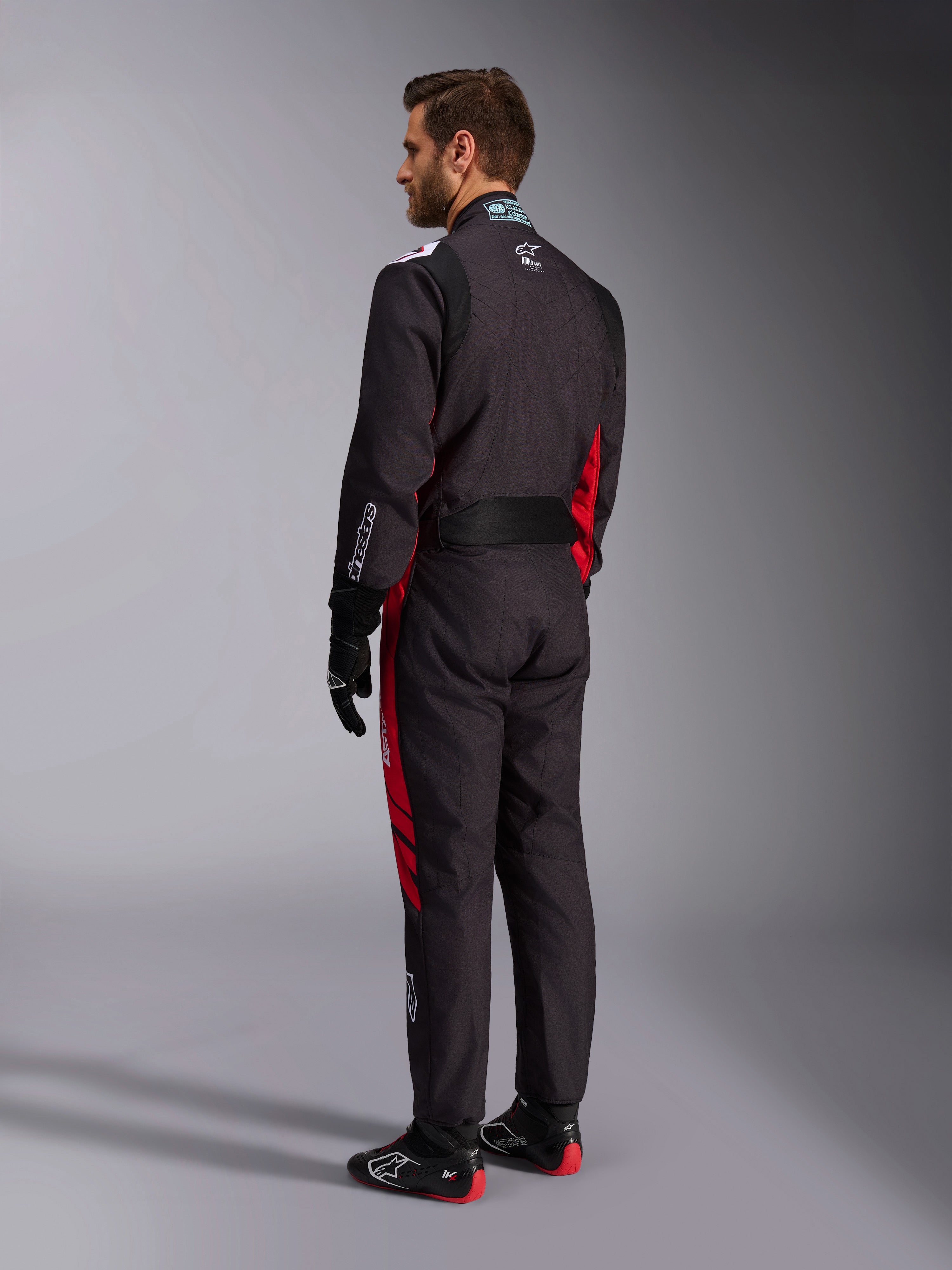 Alpinestars KMX-9 V3 Graphic 3 Suit, nero e rosso, vista posteriore del modello con attrezzatura completa da kart inclusi guanti neri e stivali da corsa, con pannelli laterali rossi e dettagli del logo bianchi