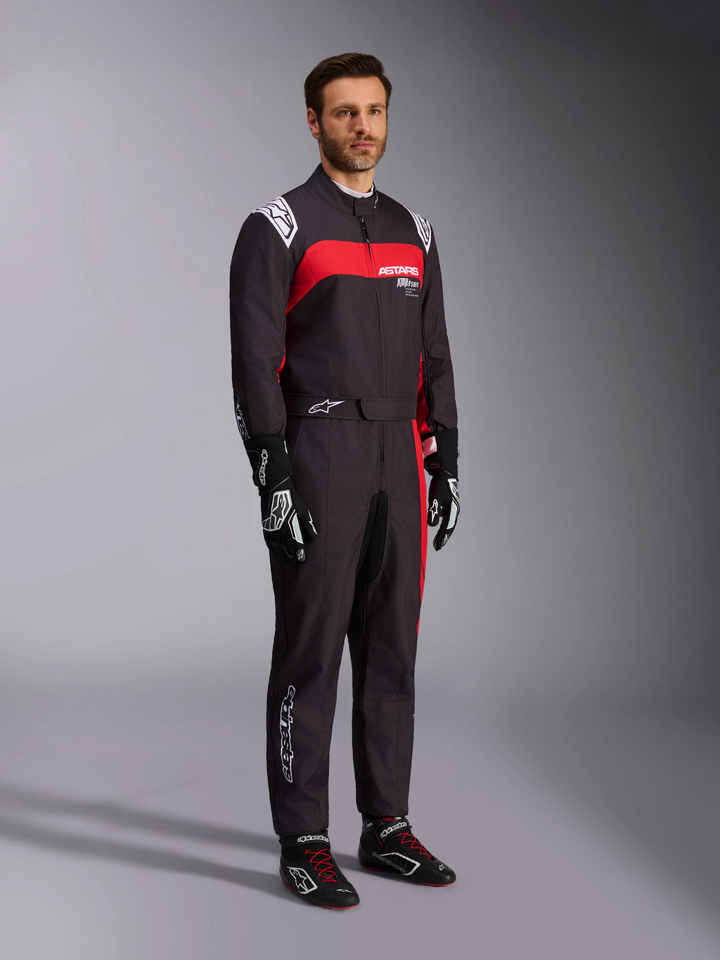 Modello che indossa la tuta Alpinestars KMX-9 V3 Graphic 3, tuta da kart, nero e rosso, con spalline bianche e logo rosso sul petto, abbinata a guanti da corsa neri e scarpe con lacci rossi, abbigliamento professionale per motorsport.