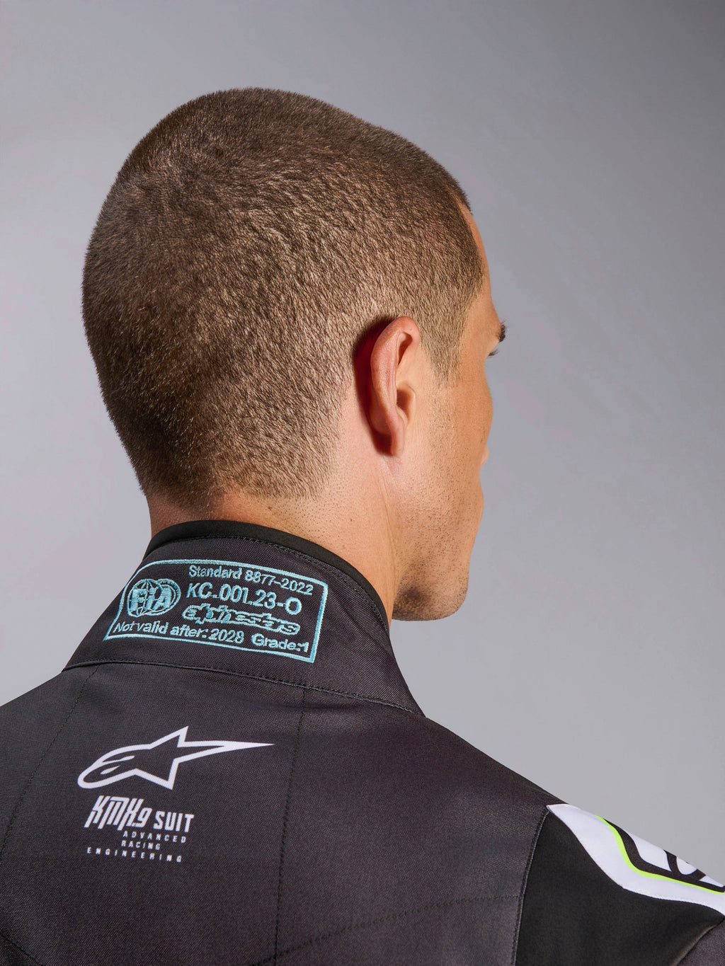 Tuta Alpinestars KMX-9 V3 Graphic 3, primo piano della zona posteriore del colletto, con etichetta di omologazione FIA 8877-2022 Grado 1 e marchio KMX-9 bianco su materiale nero, dettaglio dell'attrezzatura da karting