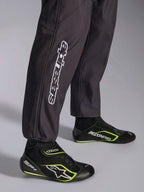 Tuta Alpinestars KMX-9 V3 Graphic 3, tuta da karting, nera, primo piano della parte inferiore delle gambe e dei polsini alle caviglie, con branding Alpinestars verticale bianco, abbinata a scarpe da karting nere e giallo fluo, dettaglio di abbigliamento professionale da karting