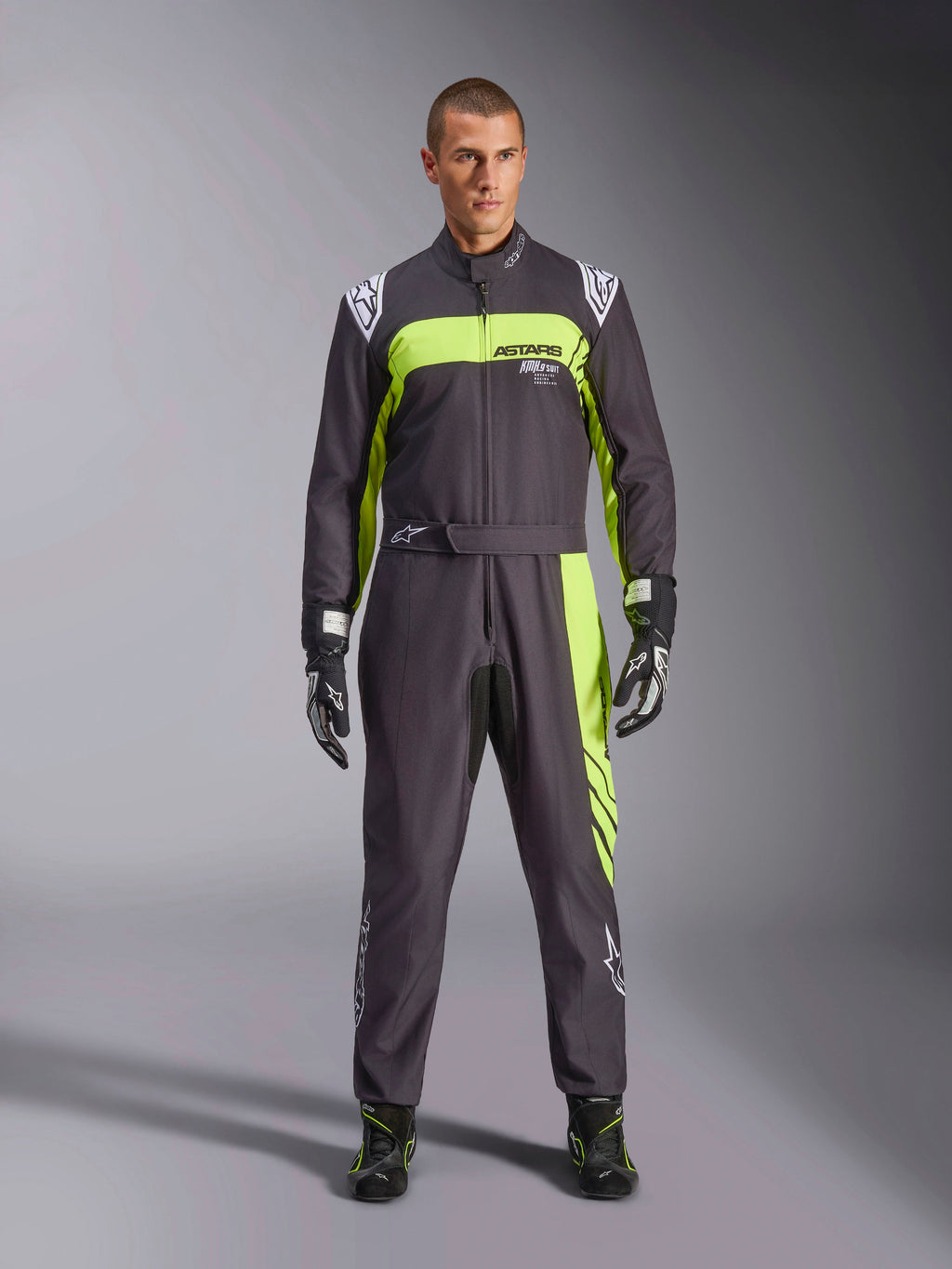 Tuta Alpinestars KMX-9 V3 Graphic 3, nero e giallo fluo, tuta da kart professionale intera indossata da un modello, con vivaci accenti giallo neon, marchio ASTARS sul petto, guanti e stivaletti da corsa abbinati