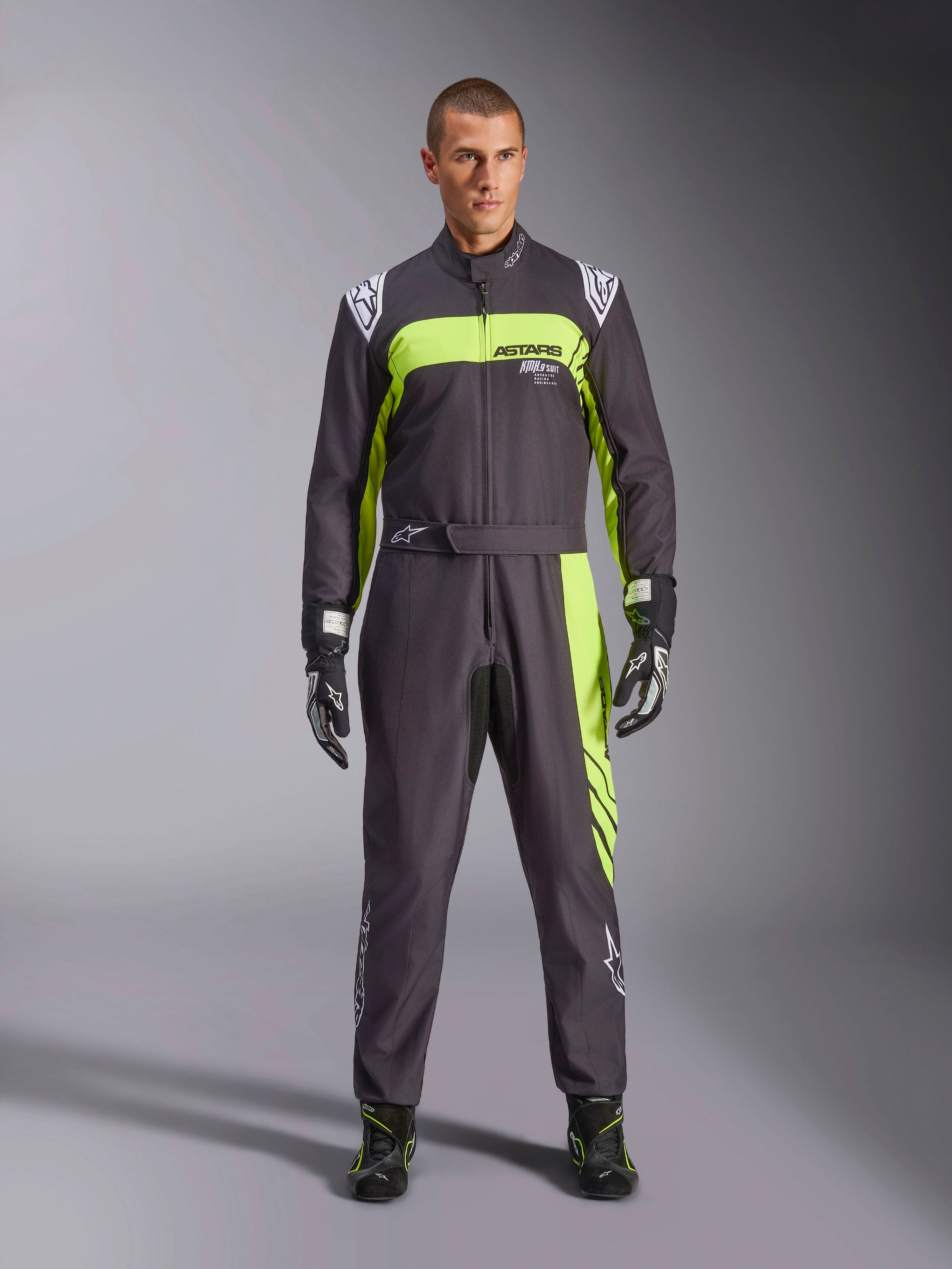 Tuta Alpinestars KMX-9 V3 Graphic 3, nero e giallo fluo, tuta da kart professionale intera indossata da un modello, con vivaci accenti giallo neon, marchio ASTARS sul petto, guanti e stivaletti da corsa abbinati