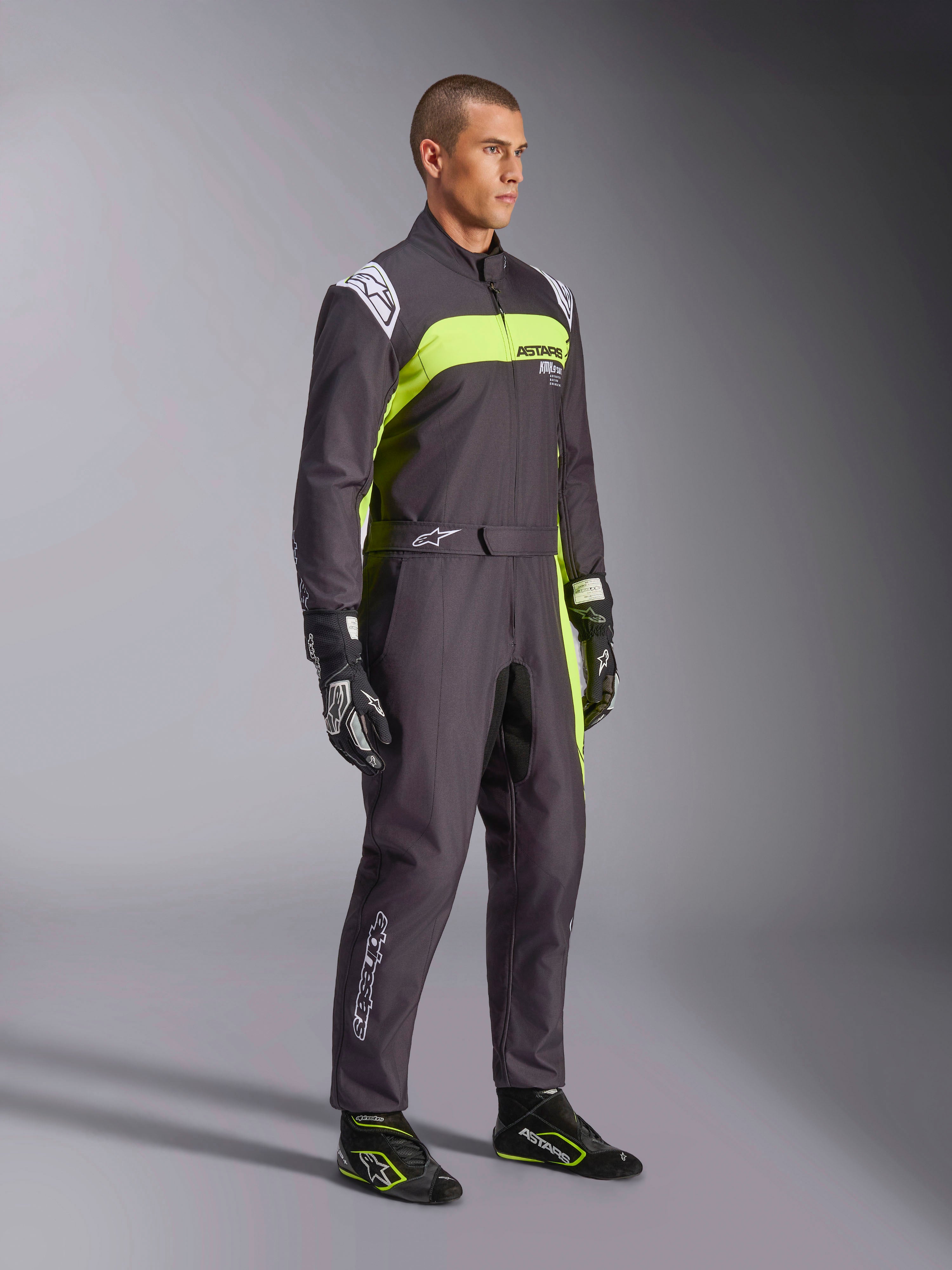 Modello con Tuta Alpinestars KMX-9 V3 Graphic 3 in nero e giallo fluo, abbigliamento professionale da karting con vivaci pannelli giallo neon e dettagli bianchi, accessoriato con guanti e scarpe da corsa coordinati, su sfondo da studio