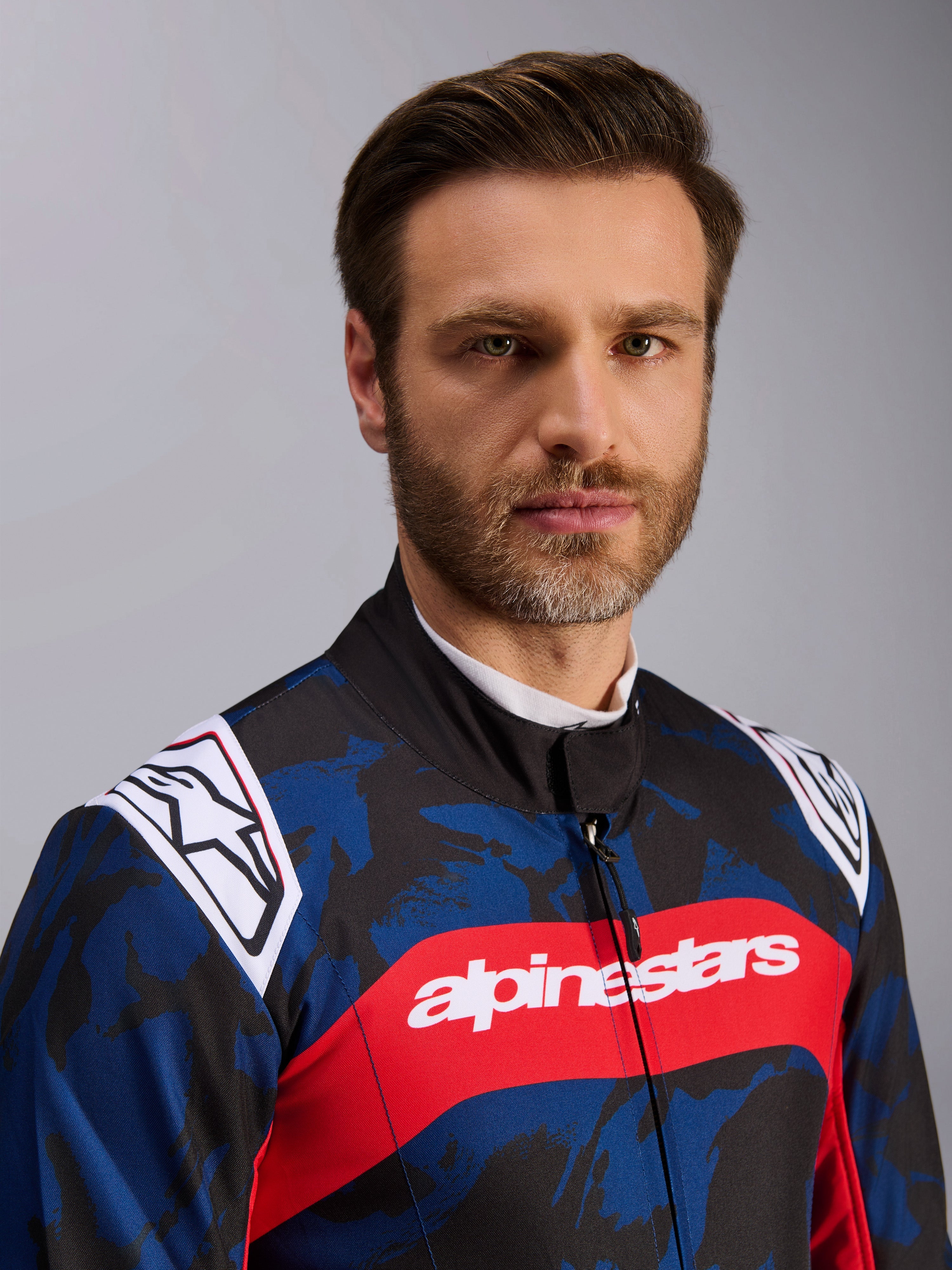 Tuta Alpinestars KMX-9 V3 Graphic 5, tuta da kart in Navy Red, con motivo grafico mimetico blu e nero, striscia orizzontale rossa con scritta alpinestars bianca sul petto e loghi bianchi sulle spalle, indossata da un modello in studio