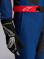 Tuta Alpinestars KMX-9 V3 Graphic 5, tuta da kart, blu navy e rosso, primo piano che mostra la cintura regolabile rossa con logo bianco, indossata con guanto da kart nero, caratterizzata da resistente tessuto blu navy e tasca sulla coscia integrata