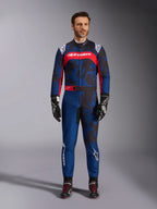 Tuta Alpinestars KMX-9 V3 Graphic 5, tuta da kart in blu navy e rosso, caratterizzata da un motivo grafico astratto in stile camo, indossata da un modello con guanti e scarpe da corsa neri, design atletico con loghi Alpinestars in evidenza su petto e gambe.