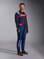 Modello che indossa la tuta Alpinestars KMX-9 V3 Graphic 5 in Navy Red, inquadratura a figura intera completa di guanti da kart neri e scarpe da corsa nere, tuta blu navy con grafiche scure stile camouflage e un pannello rosso sul petto con logo bianco, abbigliamento protettivo professionale per il karting