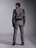 Alpinestars KMX-9 V3 Graphic 5 Suit, tuta da karting, motivo camouflage grigio scuro e nero sulla parte superiore del corpo, vista posteriore che mostra i pannelli elasticizzati e il marchio Alpinestars, indossata con guanti neri e scarpe da corsa nere con dettagli rossi, abbigliamento professionale per competizioni motoristiche