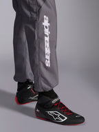 Tuta Alpinestars KMX-9 V3 Graphic 5, tuta da kart, grigio scuro, primo piano della parte inferiore della gamba con logo Alpinestars verticale bianco, indossata con scarpe da corsa nere e rosse, materiale resistente per competizioni di kart