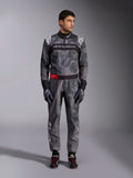 Tuta Alpinestars KMX-9 V3 Graphic 5, tuta da karting, grigio scuro e nero con grafiche in stile camouflage, con fascia nera sul petto con logo bianco e dettaglio rosso sulla cintura, indossata con guanti e scarpe da corsa coordinati, abbigliamento professionale per motorsport