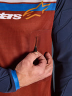 Primo piano della maglia Alpinestars Maxdura Dual, busto in mesh Rust Brown con tasca sul petto senza cuciture con cerniera, maniche Mood Indigo con imbottitura integrata, dettaglio tecnico di maglia da moto adventure