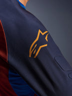 Alpinestars Maxdura Dual Jersey, primo piano della manica Mood Indigo con logo Alpinestars giallo, che mostra l'imbottitura in mesh distanziatore integrata e il tessuto a rete del busto color Rust Brown, abbigliamento tecnico da moto adventure