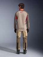 Alpinestars Maxdura Dual Jersey in Aluminum Walnut, vista posteriore, torso in mesh color sabbia con maniche marroni e loghi rossi, bordo posteriore allungato, abbinata a pantaloni da adventure e stivali neri.
