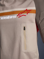Alpinestars Maxdura Dual Jersey, Aluminum Walnut, dettaglio ravvicinato del busto in rete, striscia orizzontale arancione e bianca con logo rosso, tasca pettorale verticale con cerniera, abbigliamento da moto adventure