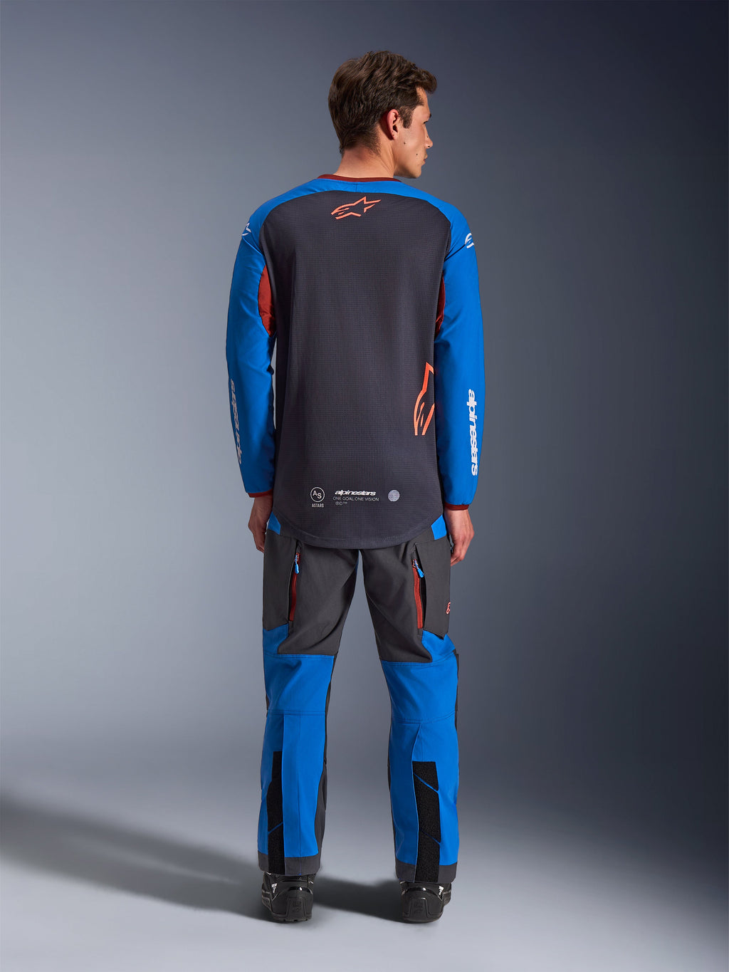 Alpinestars Maxdura Dual Jersey in grigio scuro e blu reale, vista posteriore con busto in mesh e logo a stella arancione, maniche blu reale con scritte bianche, abbinata a pantaloni adventure grigi e blu, abbigliamento ad alte prestazioni per guida dual-sport
