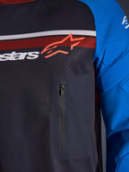 Alpinestars Maxdura Dual Jersey, primo piano di petto e manica, Deep Gray e Royal Blue, con tasca sul petto con cerniera, busto in mesh traspirante e imbottitura integrata sulle maniche, logo Alpinestars su strisce rosse e bianche.