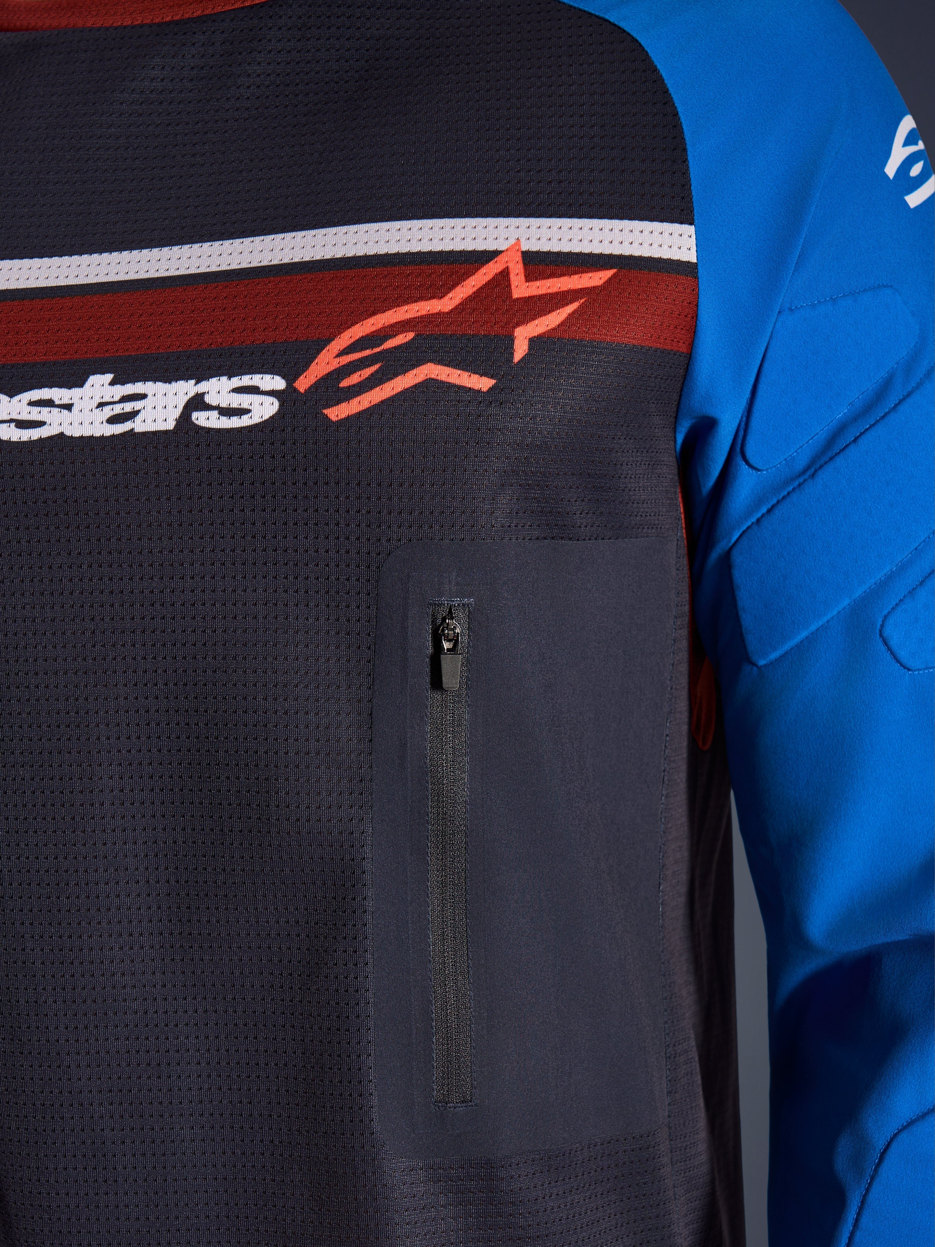 Alpinestars Maxdura Dual Jersey, primo piano di petto e manica, Deep Gray e Royal Blue, con tasca sul petto con cerniera, busto in mesh traspirante e imbottitura integrata sulle maniche, logo Alpinestars su strisce rosse e bianche.