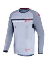 Alpinestars Maxdura Dual Jersey, maglia da moto adventure, grigio medio e grigio scuro, vista frontale con tasche sul petto con zip verticali, maniche resistenti all'abrasione con imbottitura integrata, logo Alpinestars in rosso e bianco, abbigliamento tecnico per guida fuoristrada