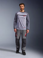 Alpinestars Maxdura Dual Jersey, grigio medio e grigio scuro, maglia da moto adventure con torso in rete e tasche sul petto con cerniera, maniche resistenti all'abrasione con imbottitura integrata, indossata con pantaloni tecnici grigi coordinati con dettagli rossi, abbigliamento tecnico per fuoristrada