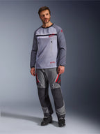 Un uomo che indossa la Alpinestars Maxdura Dual Jersey in Grigio Medio e Grigio Scuro, abbinata a pantaloni adventure coordinati grigi e neri e stivali neri, caratterizzata da un torso in rete traspirante, tasche sul petto con cerniera e dettagli del logo rossi.