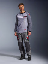 Un uomo che indossa la Alpinestars Maxdura Dual Jersey in Grigio Medio e Grigio Scuro, abbinata a pantaloni adventure coordinati grigi e neri e stivali neri, caratterizzata da un torso in rete traspirante, tasche sul petto con cerniera e dettagli del logo rossi.