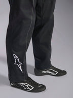 Alpinestars Kart Indoor V2 Suit, tuta da kart nera, primo piano della parte inferiore delle gambe e dei piedi con logo Alpinestars bianco sul polpaccio, abbinata a scarpe da corsa bianche e nere coordinate, progettata per il karting ricreativo.