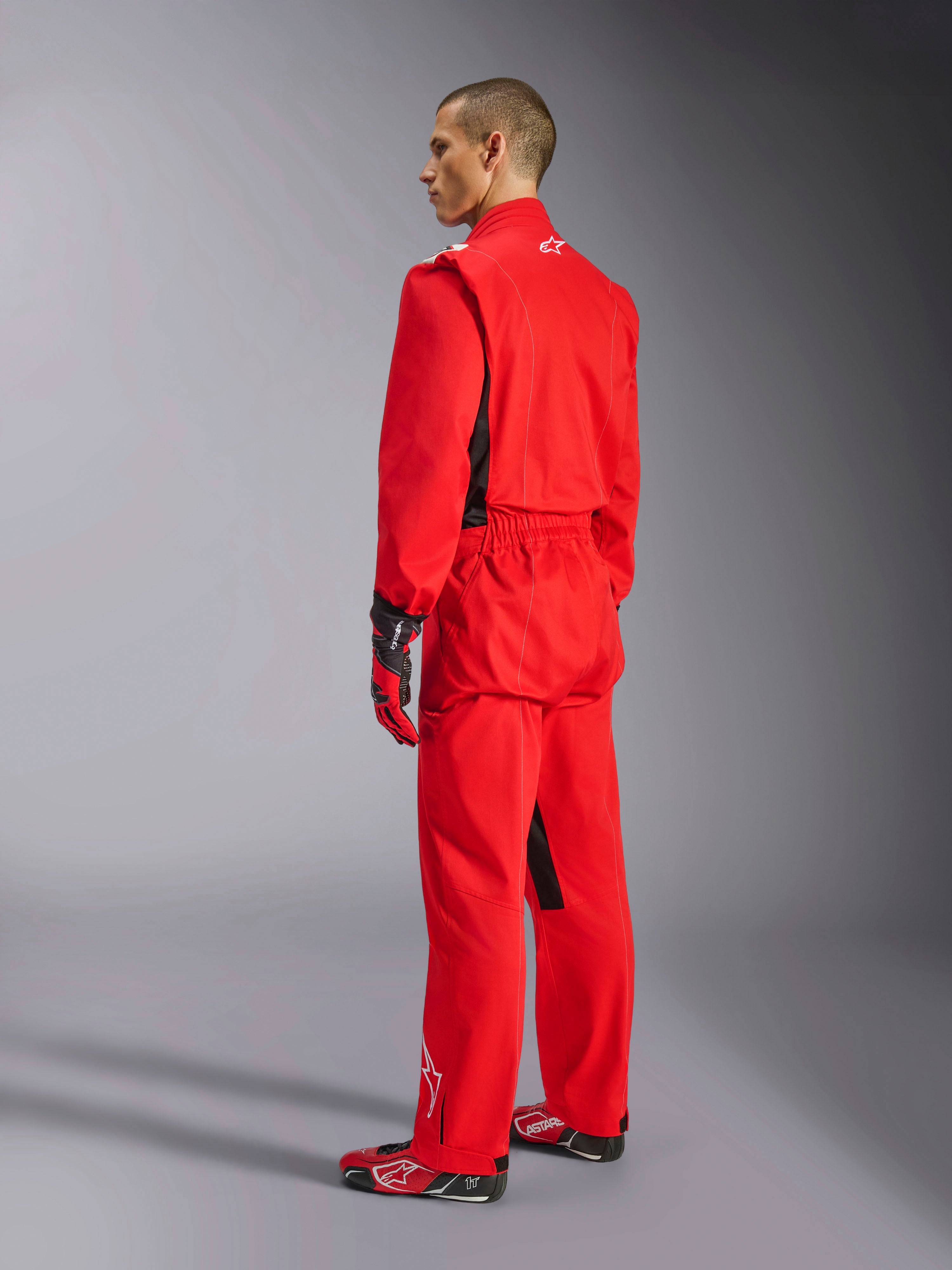 Alpinestars Kart Indoor V2 Suit, tuta da kart rossa, vista posteriore di tre quarti su un modello, indossata con guanti rossi coordinati e scarpe da corsa, costruzione in twill di policotone a strato singolo, equipaggiamento professionale da motorsport per il karting indoor.
