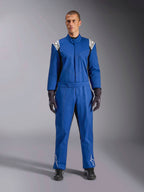 Modello che indossa la tuta Alpinestars Kart Indoor V2 in blu, tuta da kart intera con loghi a stella bianchi su spalle e stinchi, cuciture a contrasto bianche, cintura elastica in vita, abbinata a guanti da corsa e calzature neri, progettata per l'uso ricreativo in pista