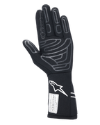 Guanti Alpinestars Tech-1 Start V4 FIA, guanto da auto racing nero, vista del palmo con motivi in silicone grigio su dita e palmo, logo Astars bianco sul polsino allungato, etichetta di certificazione FIA, attrezzatura professionale per motorsport