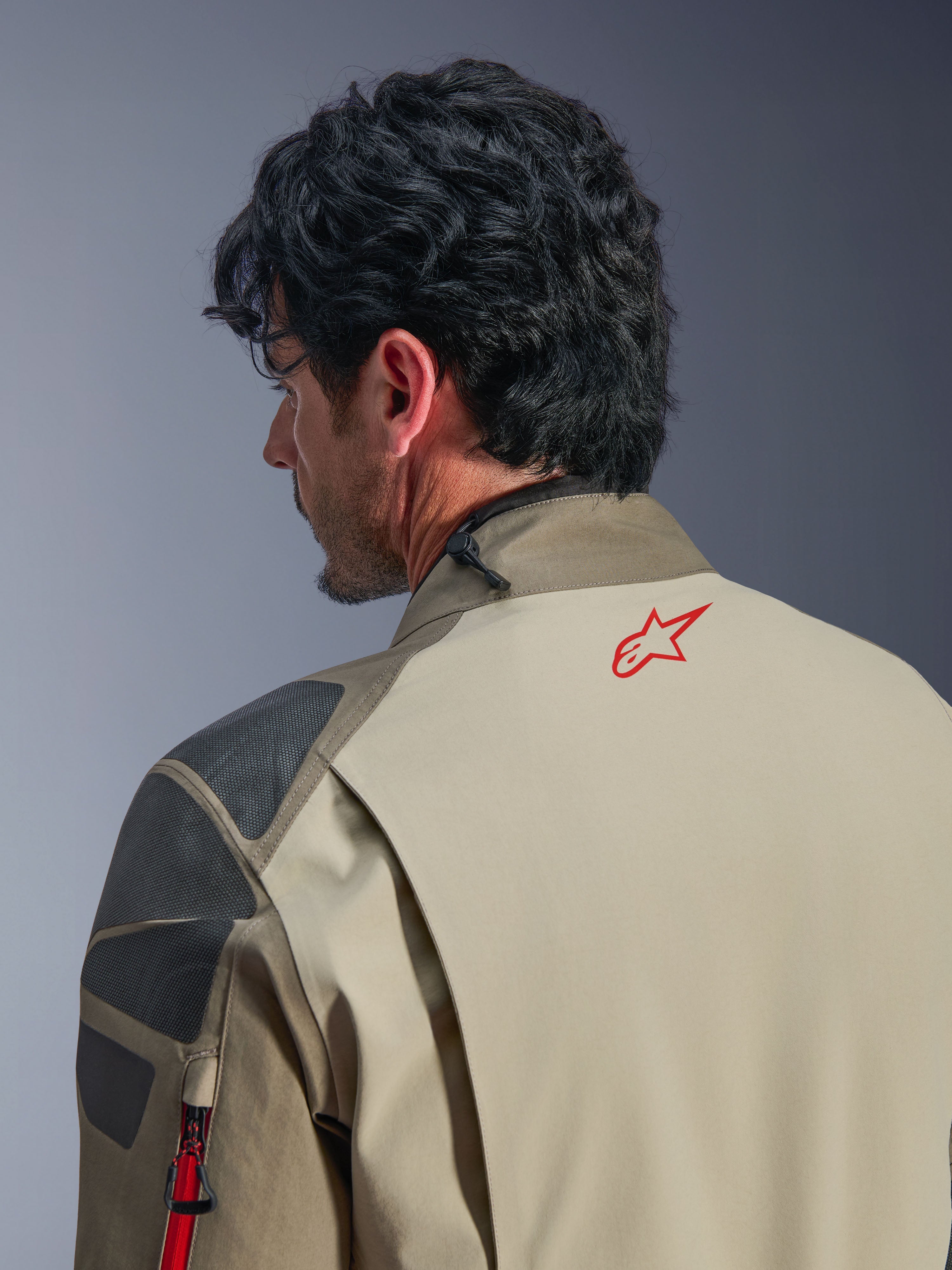 Giacca Alpinestars Nazca 3L GORE-TEX PRO, giacca da avventura Walnut Rock Brown, primo piano della schiena e della spalla, logo a stella rosso sul collo, pannelli di rinforzo grigi testurizzati, costruzione in tessuto resistente per la guida in moto