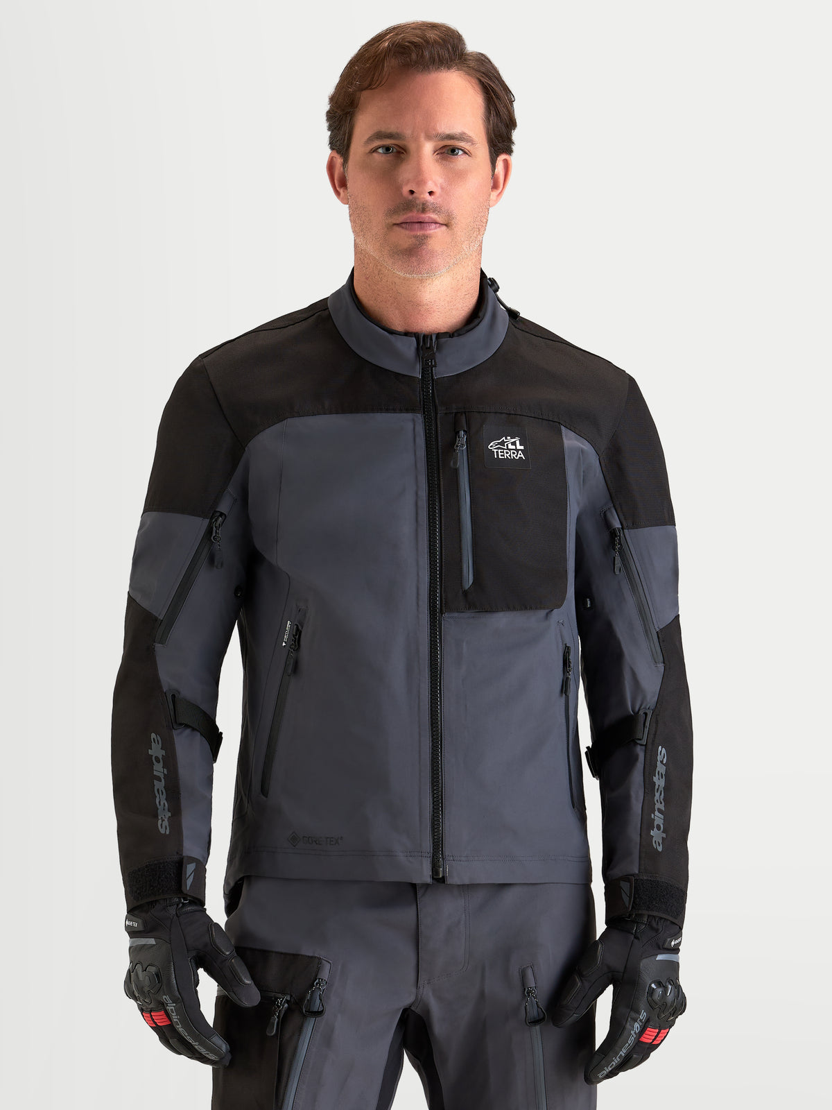 Alpinestars Arenis Gore Tex Giacca, giacca da moto adventure da uomo, nero e grigio scuro, vista frontale su un modello che indossa guanti coordinati, abbigliamento da guida impermeabile certificato AA