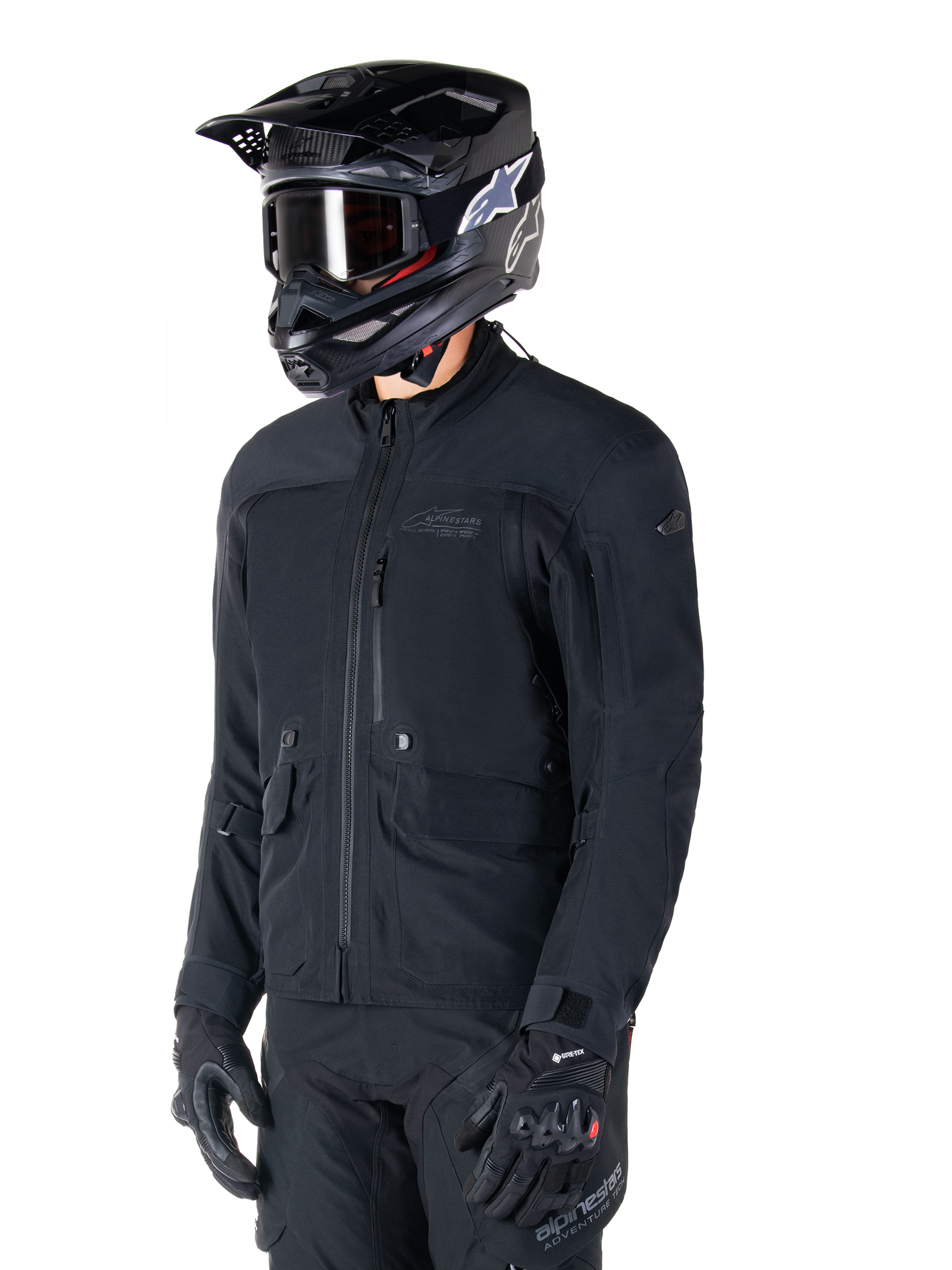 Giacca Alpinestars St-7 Prime GORE-TEX, giacca da moto nera, indossata da un pilota con casco e occhiali neri, dotata di ampie tasche cargo sul petto e guscio impermeabile laminato, abbigliamento premium per adventure touring e commuting